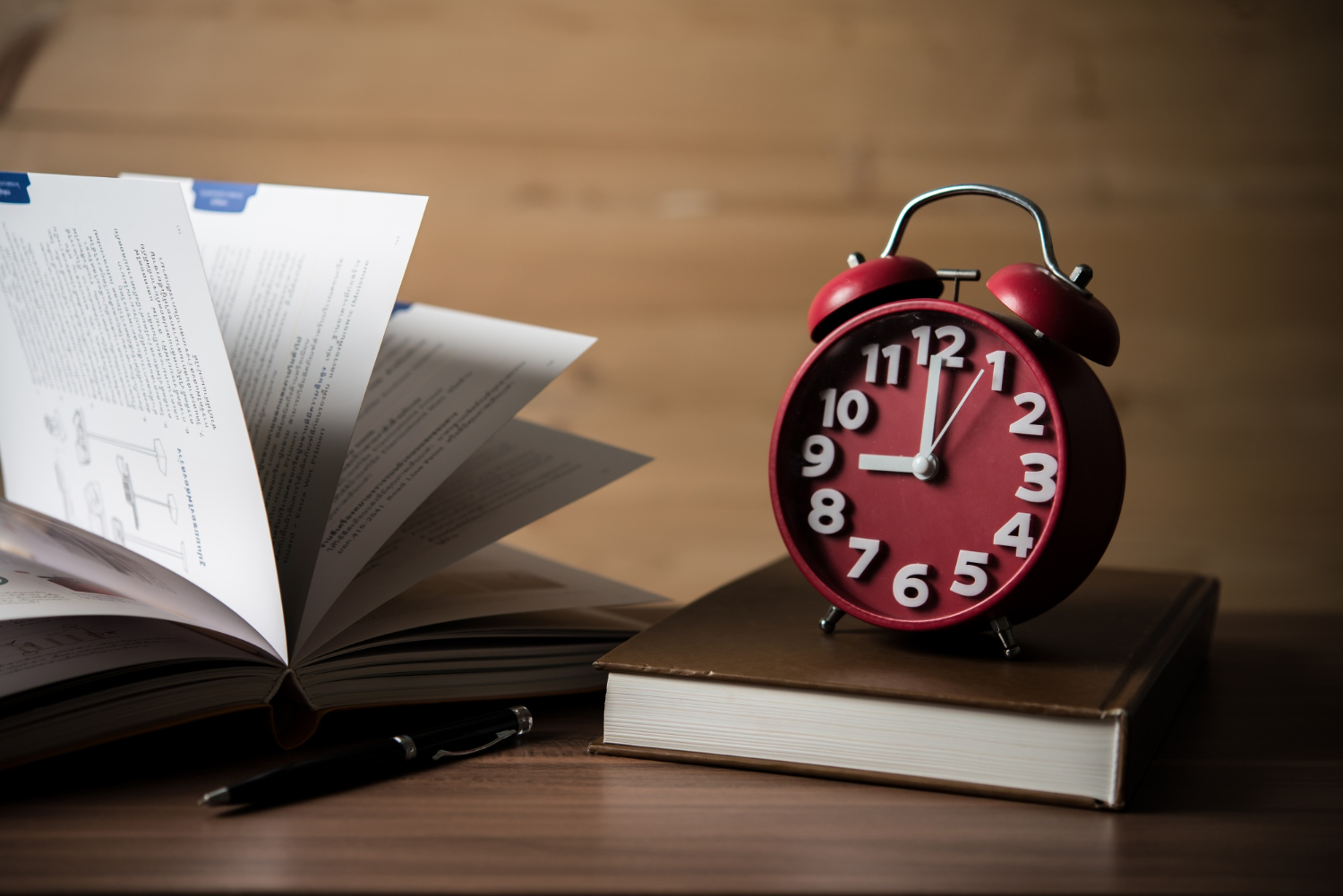 Open book, pen, and red alarm clock on a desk. Pomodoro technique to improve concentration and focus.