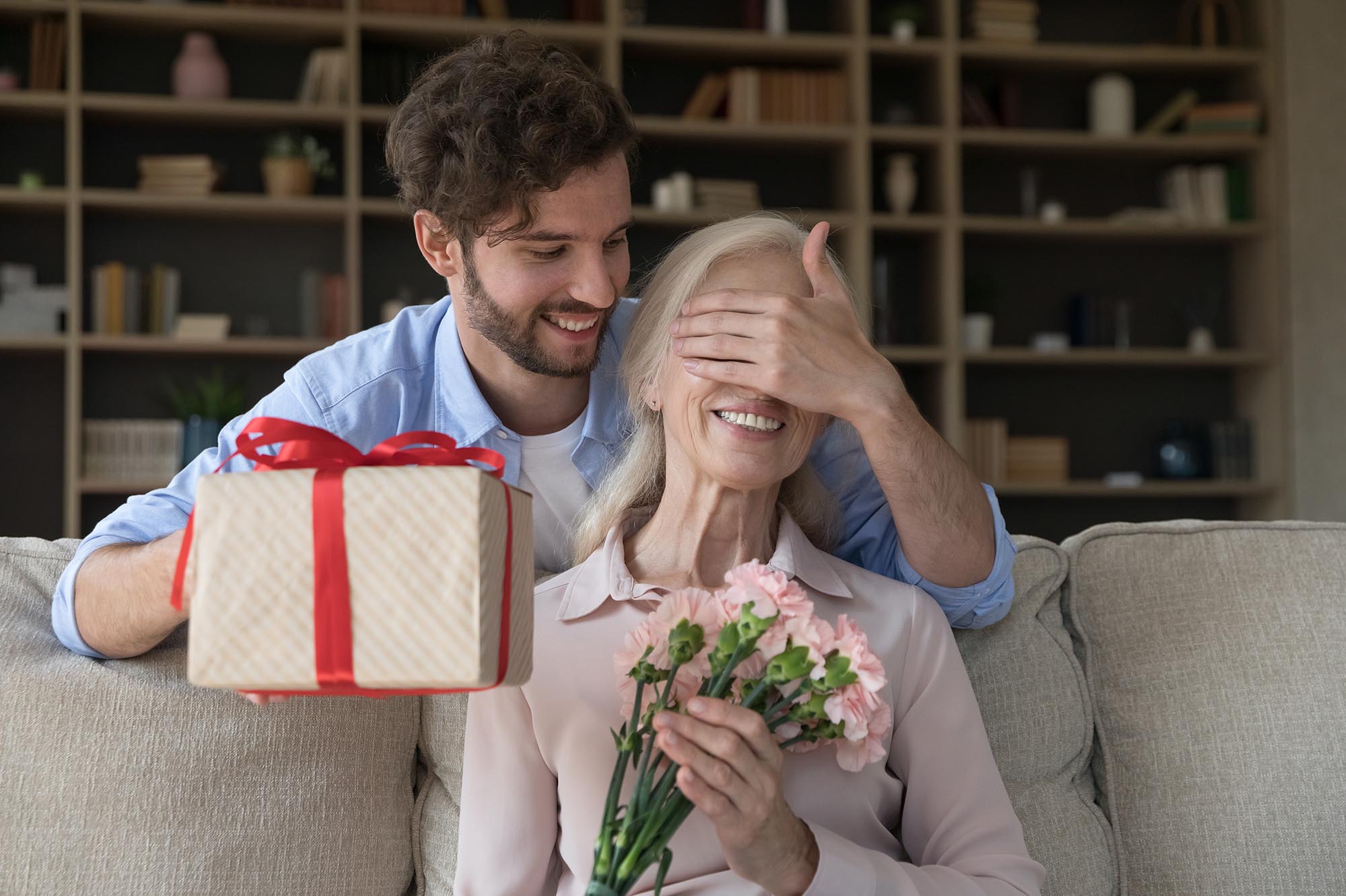 Son showing gratitude with a surprise gift and flowers for his mother.