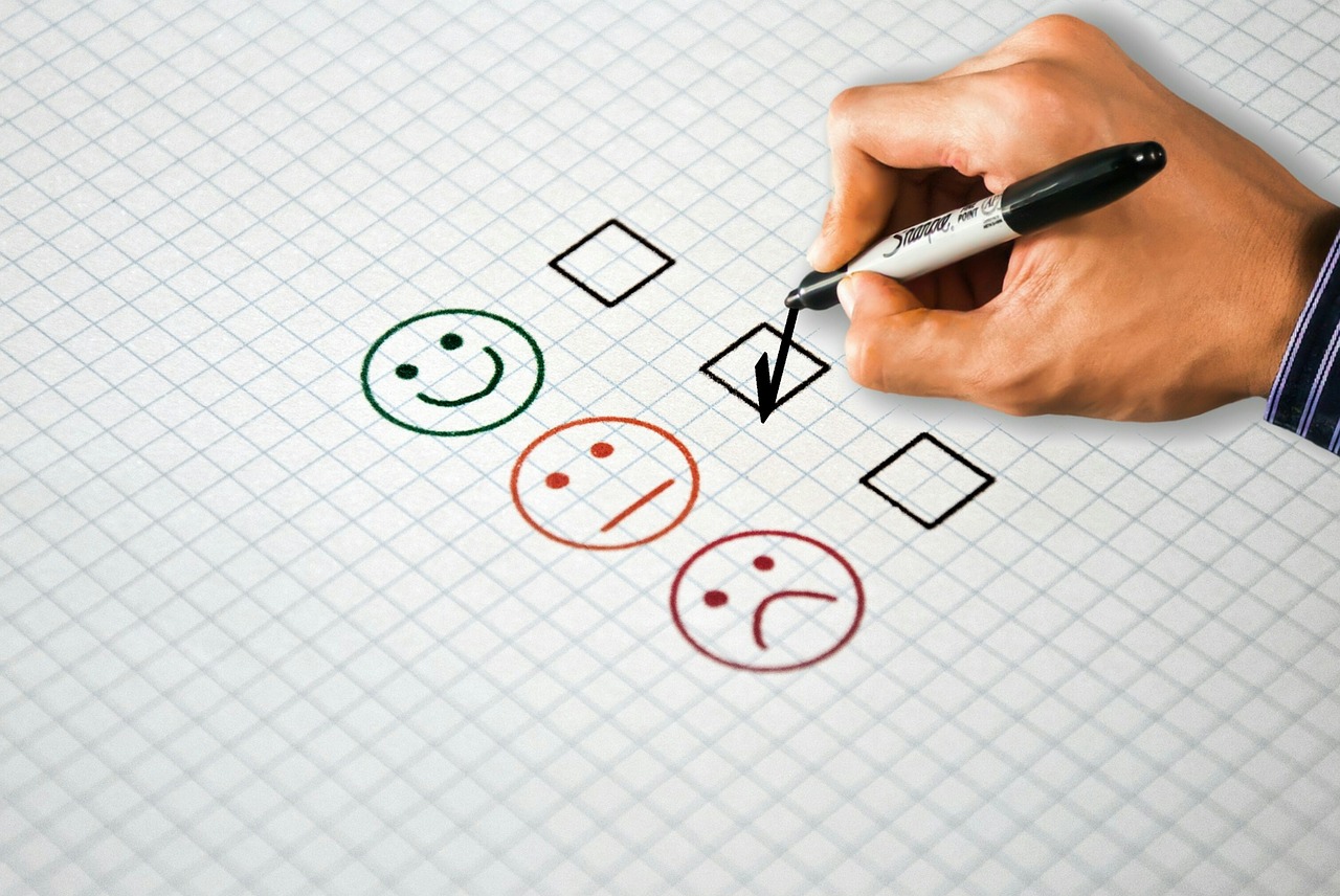 Hand marking a feedback form with happy, neutral, and sad faces, showing a key feature of constructive feedback 