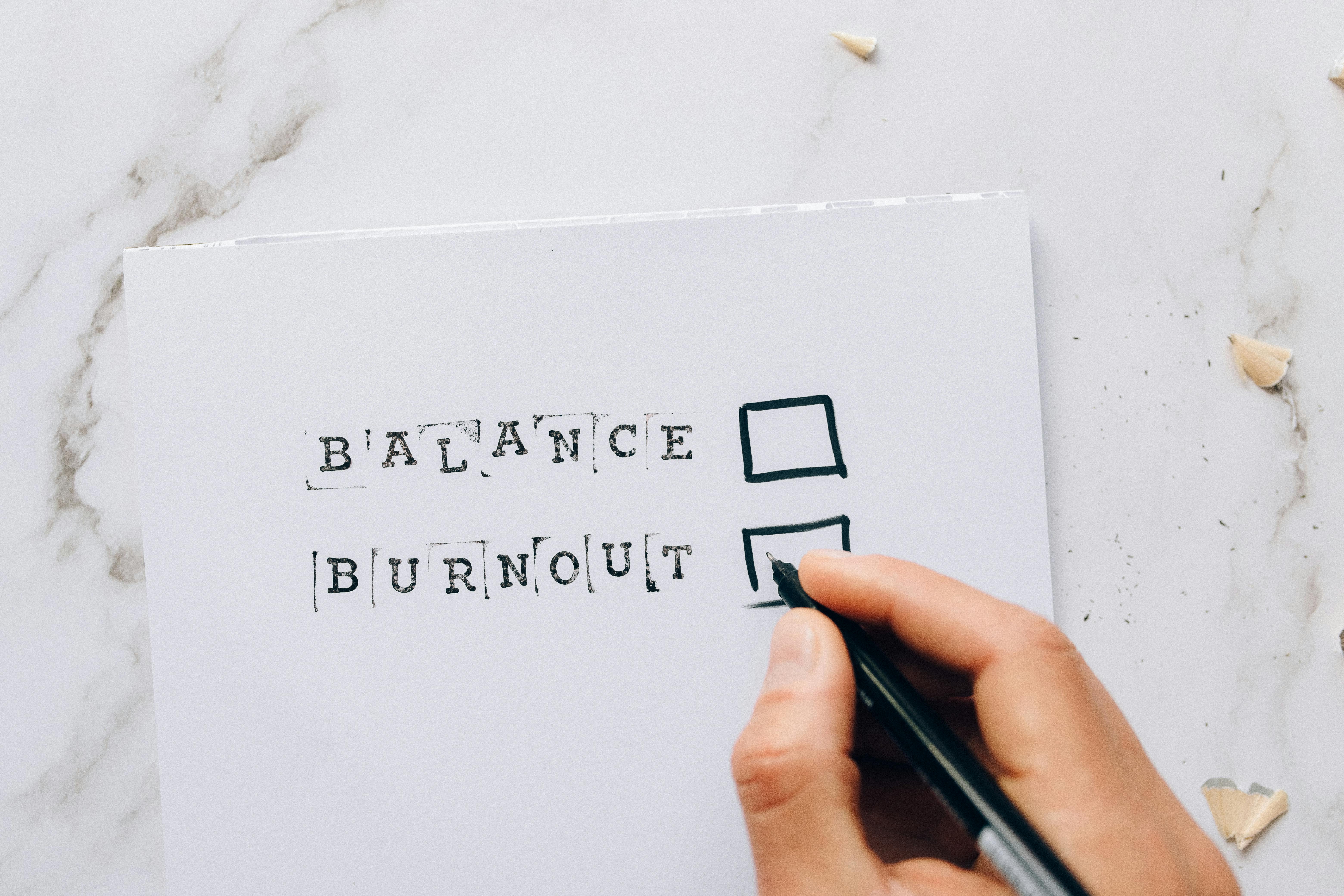 A hand drawing checkboxes next to the words “Balance” and “Burnout,” highlighting the importance of maintaining wellbeing while pursuing career goals.