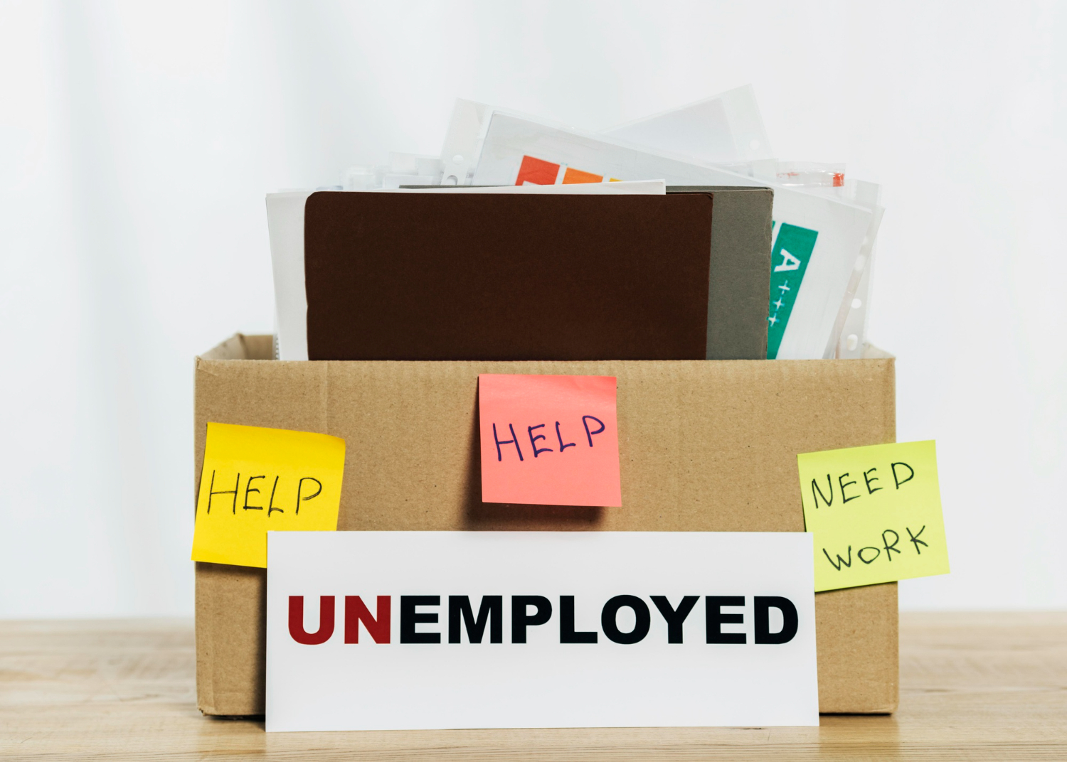 Cardboard box with office files and sticky notes reading “help” and “need work” for career change