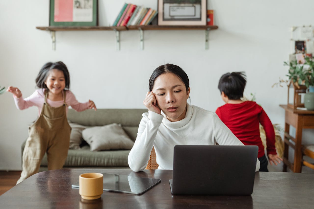 Woman working on a laptop with children in the background, showing daily anxiety triggers